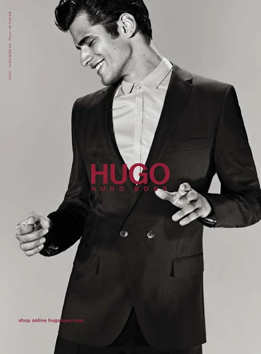 Man in a suit smiles in a fashion shot for Hugo Boss, showcasing a black double-breasted suit and a white button-down shirt.