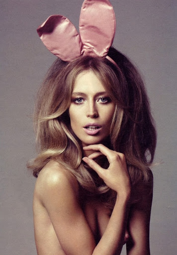 Glamour headshot of woman with blonde hair wearing pink bunny ears and bare shoulders in a studio, eye-level angle.