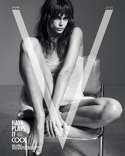 Black and white fashion shot of Kaia Gerber, seated on a chair, gazing at the camera with a neutral expression, stylish and elegant.