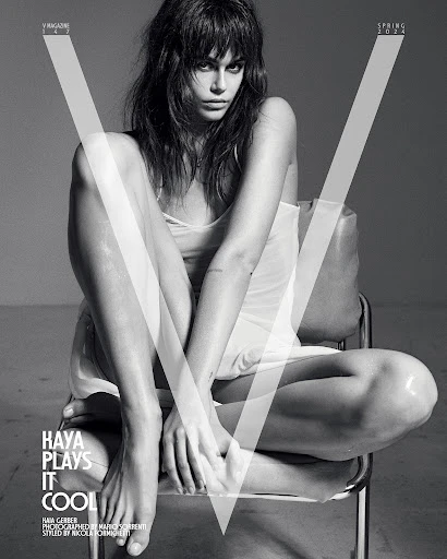 Black and white fashion shot of Kaia Gerber, seated on a chair, gazing at the camera with a neutral expression, stylish and elegant.