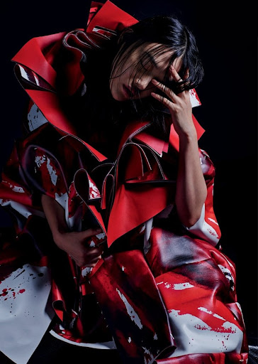 High-fashion portrait of an adult female model with dark hair wearing a voluminous red and white dress in a studio setting.