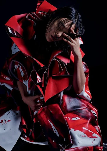 High-fashion portrait of an adult female model with dark hair wearing a voluminous red and white dress in a studio setting.