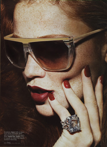 Close-up shot of a fair-skinned adult female model with red hair, wearing sunglasses, red lipstick, and a large diamond ring.