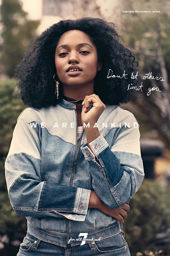 Portrait of a mixed-race woman with afro wearing a denim jacket, posing outdoors in a fashion editorial shot with natural lighting and a blurred background.