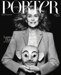 Monochrome portrait of Lauren Hutton holding a carved mask wearing a blazer against a dark background