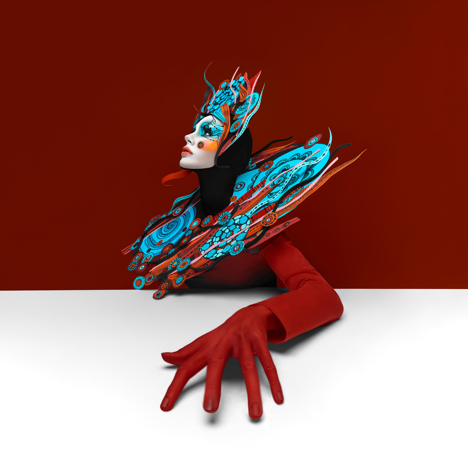 Artistic studio portrait of a woman with elaborate makeup and a teal headdress against a dark red background with a white foreground.