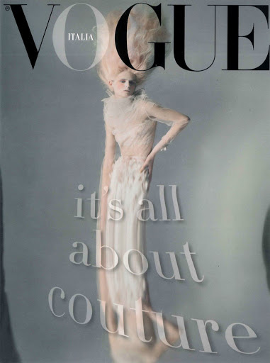 Vogue Italia cover featuring a pale-skinned woman in a light-colored, high-fashion gown and elaborate headpiece against a soft grey background.