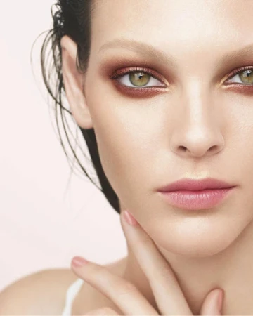 Close-up beauty portrait of a woman with green eyes, glossy pink lips, and natural makeup against a soft white background.