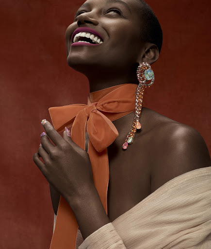 Close-up of a smiling African-American woman wearing a large jeweled earring and an orange velvet bow against a red background.