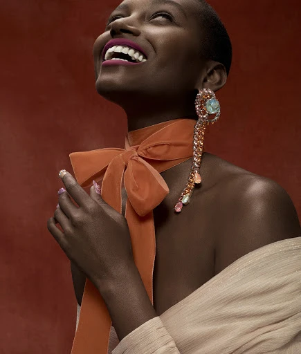 Close-up of a smiling African-American woman wearing a large jeweled earring and an orange velvet bow against a red background.