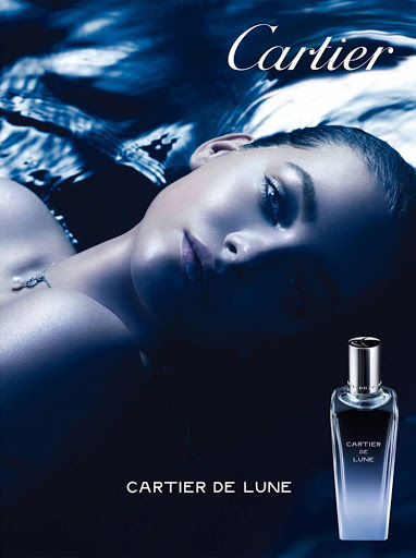 Elegant beauty advertisement for Cartier de Lune perfume featuring a woman reclining and a bottle of perfume on a blue background.
