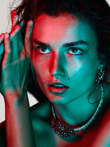 Close-up studio portrait of a young woman with dark hair and jeweled necklace, illuminated by contrasting red and teal lighting.