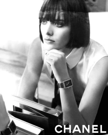 Monochrome portrait of a woman with a blunt bob haircut resting her chin on her hand, wearing a wristwatch.