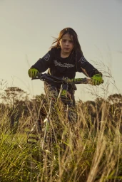 Young child riding a mountain bike through tall grass outdoors during late afternoon golden hour light.
