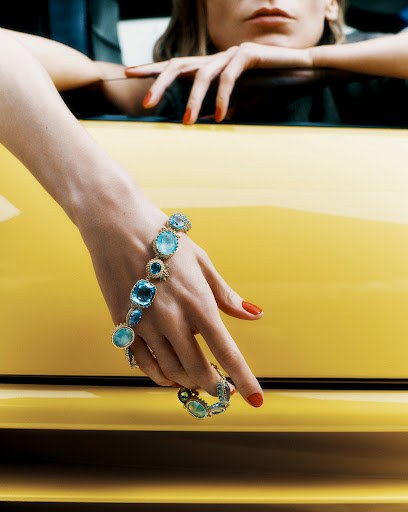 Woman's hand with red nails displays a blue gemstone bracelet on a yellow car; the image is a close-up with a shallow depth of field.