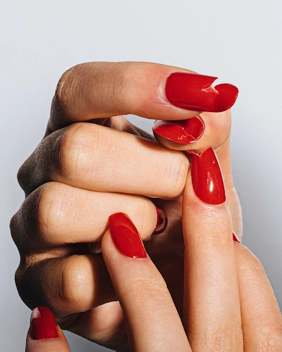 Close-up of a light-skinned adult female hand with a red manicure, one nail broken, against a light neutral background in a studio shot.