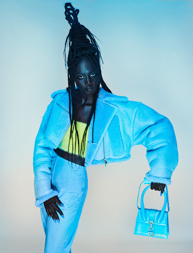 Woman in cyan shearling jacket and matching pants holding a small cyan purse poses against a neutral background in a studio shot.