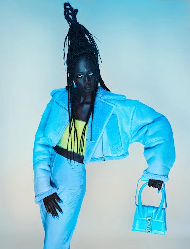 Woman in cyan shearling jacket and matching pants holding a small cyan purse poses against a neutral background in a studio shot.