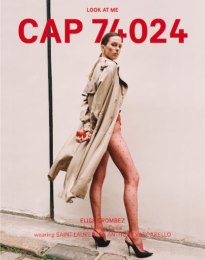 Fashion editorial shot of a female model wearing a beige trench coat and high heels, holding a red apple in front of a beige wall.