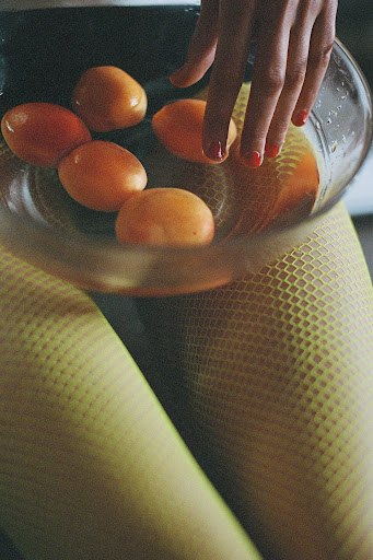Close-up of woman's hand reaching into a glass bowl filled with five apricots. She is wearing bright yellow textured tights.
