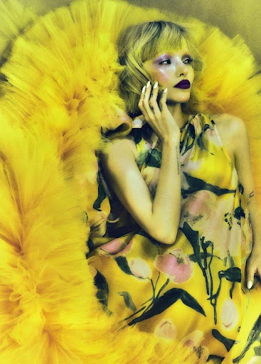Artistic portrait of a woman with striking makeup and a yellow floral gown, against a soft, diffused background, evoking high fashion.
