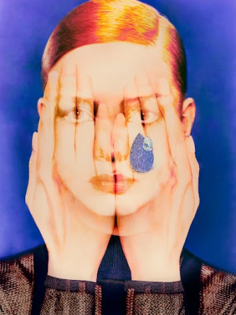 Conceptual portrait of a person obscuring their face with hands, featuring a blue gemstone teardrop and colorful hair against a blue backdrop.