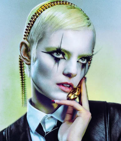 Close-up portrait of a model with dramatic graphic eye makeup, bleached short hair, wearing a white collared shirt and black jacket.
