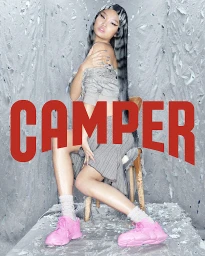 Asian woman with long grey and black striped hair sitting on a rustic wooden chair wearing pink sneakers against a crumpled foil background