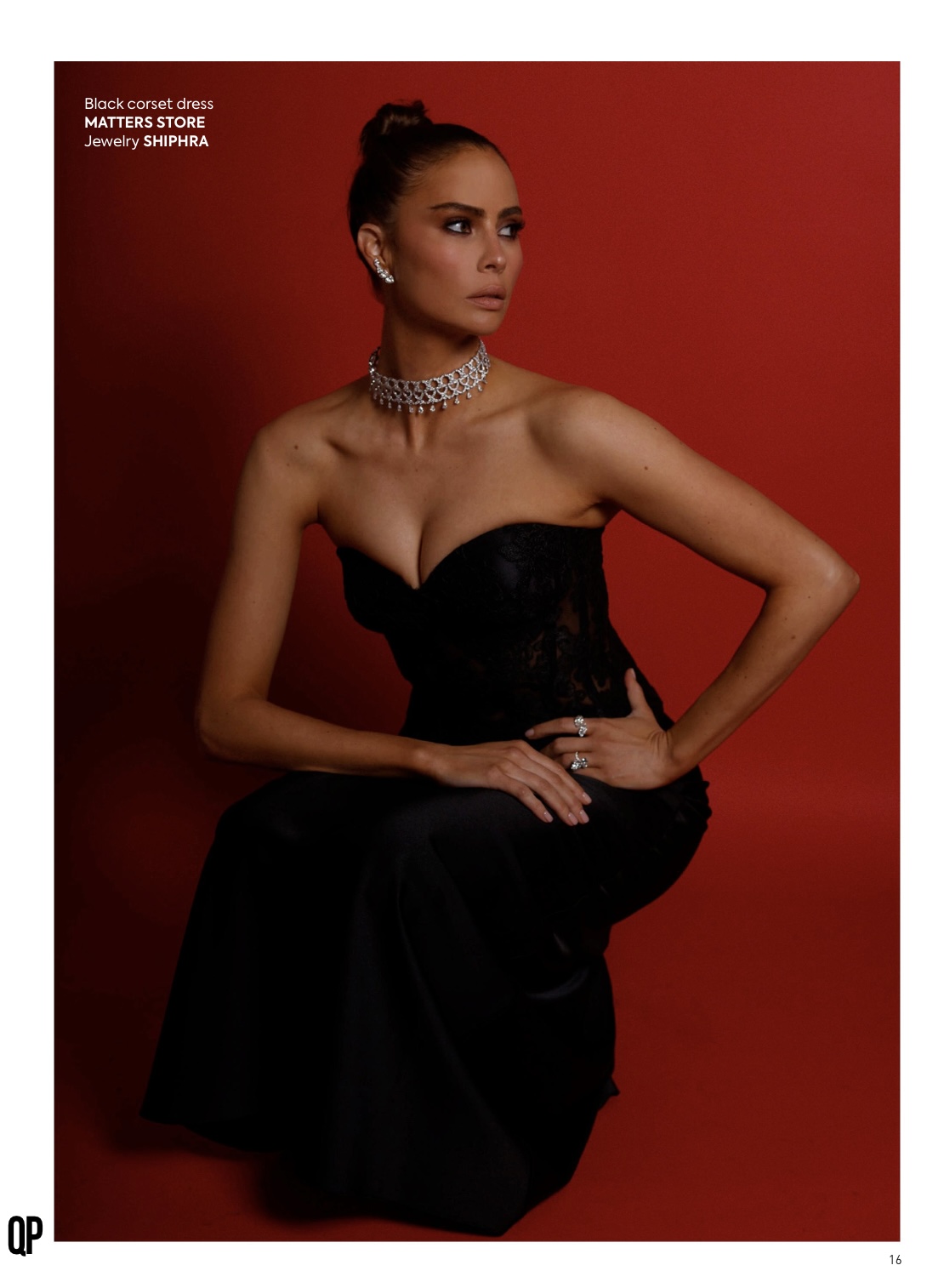 Elegant woman in a black corset dress and diamond jewelry poses against a red studio backdrop, fashion photography, beauty shot.