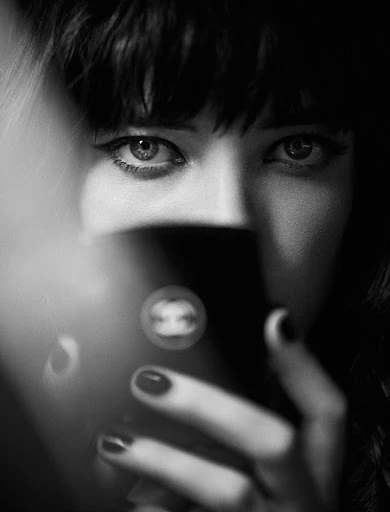 Black-and-white portrait of an adult female with bangs and dark manicure, holding a shiny black case with Chanel logo.