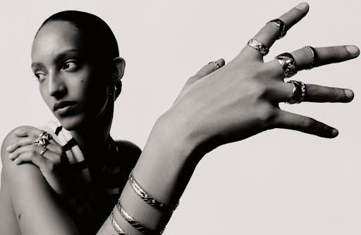 Close-up portrait of a model with numerous silver rings and bangles, featuring nail art by Julie Villanova against a white backdrop