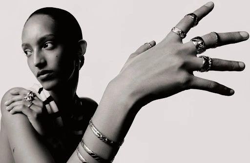 Close-up portrait of a model with numerous silver rings and bangles, featuring nail art by Julie Villanova against a white backdrop