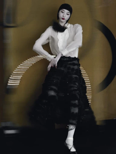 A woman in a vintage-style dress and cap poses against a textured gold backdrop with circular lighting, creating a retro fashion portrait.
