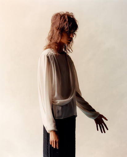 Portrait of a woman in a cream-colored blouse and a dark skirt posing in front of an off-white background in a studio setting.