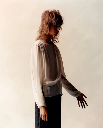 Portrait of a woman in a cream-colored blouse and a dark skirt posing in front of an off-white background in a studio setting.