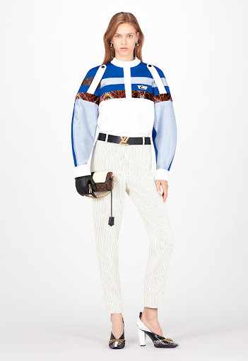 Full-length shot of an adult female fashion model in a studio, wearing a blue and white patterned top with pinstripe pants and patterned heels.