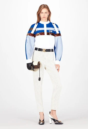 Full-length shot of an adult female fashion model in a studio, wearing a blue and white patterned top with pinstripe pants and patterned heels.