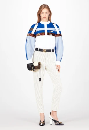 Full-length shot of an adult female fashion model in a studio, wearing a blue and white patterned top with pinstripe pants and patterned heels.