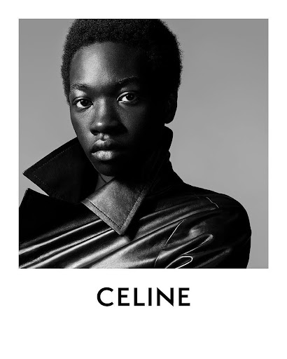 Black and white portrait of a dark-skinned male model wearing a black leather coat in front of a gray backdrop with CELINE text.