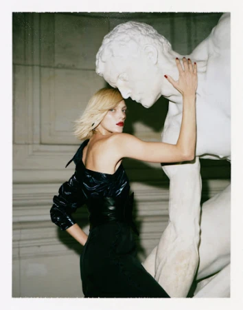 Blonde woman with red lipstick leaning against a white marble statue in a museum interior with polaroid border
