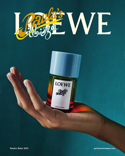 An open hand holds a colorful LOEWE perfume bottle against a dark teal wall with bold white typography above.