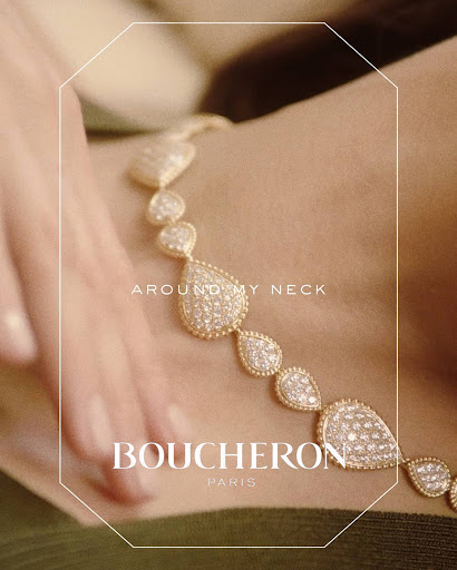 Close-up of a diamond and gold necklace around a neck with a hand resting nearby, featuring Boucheron Paris text.