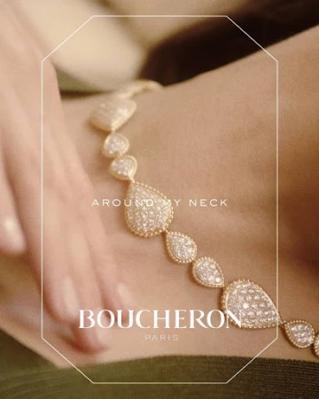 Close-up of a diamond and gold necklace around a neck with a hand resting nearby, featuring Boucheron Paris text.