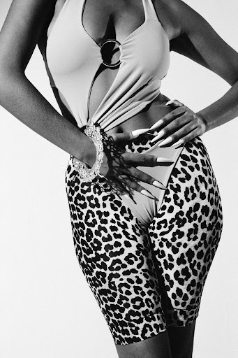 Monochrome portrait of a woman in a cutout bodysuit and leopard print shorts, featuring a bracelet and long nails.