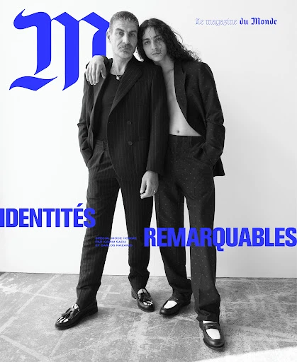 Magazine cover featuring two men in suits standing indoors; one arm around the other's shoulder; bold blue typography on a white background.