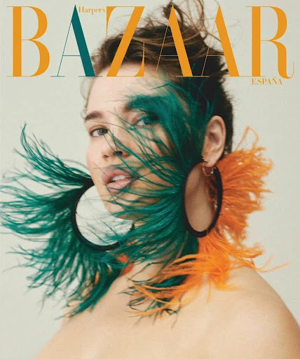 Glamorous fashion magazine cover featuring a woman with feathered earrings, wearing minimal makeup and a neutral-toned top, in a close-up.