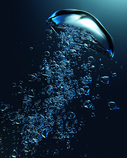 Close-up studio shot of numerous translucent blue bubbles rising against a dark blue gradient background, creating an abstract underwater effect.