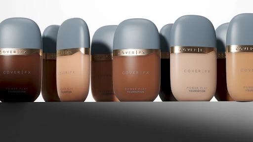 An array of nine cosmetic foundation bottles featuring varying skin tone shades with grey caps on a white surface.