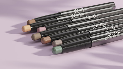 Group of Julep brand eyeshadow sticks in various colors with black packaging, arranged on a lilac surface under soft lighting.