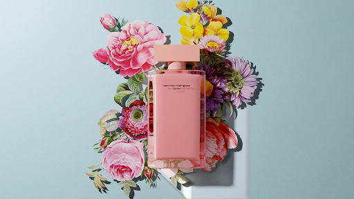 Still life photo of a light pink Narciso Rodriguez perfume bottle, surrounded by an arrangement of colorful flowers on a light blue background.